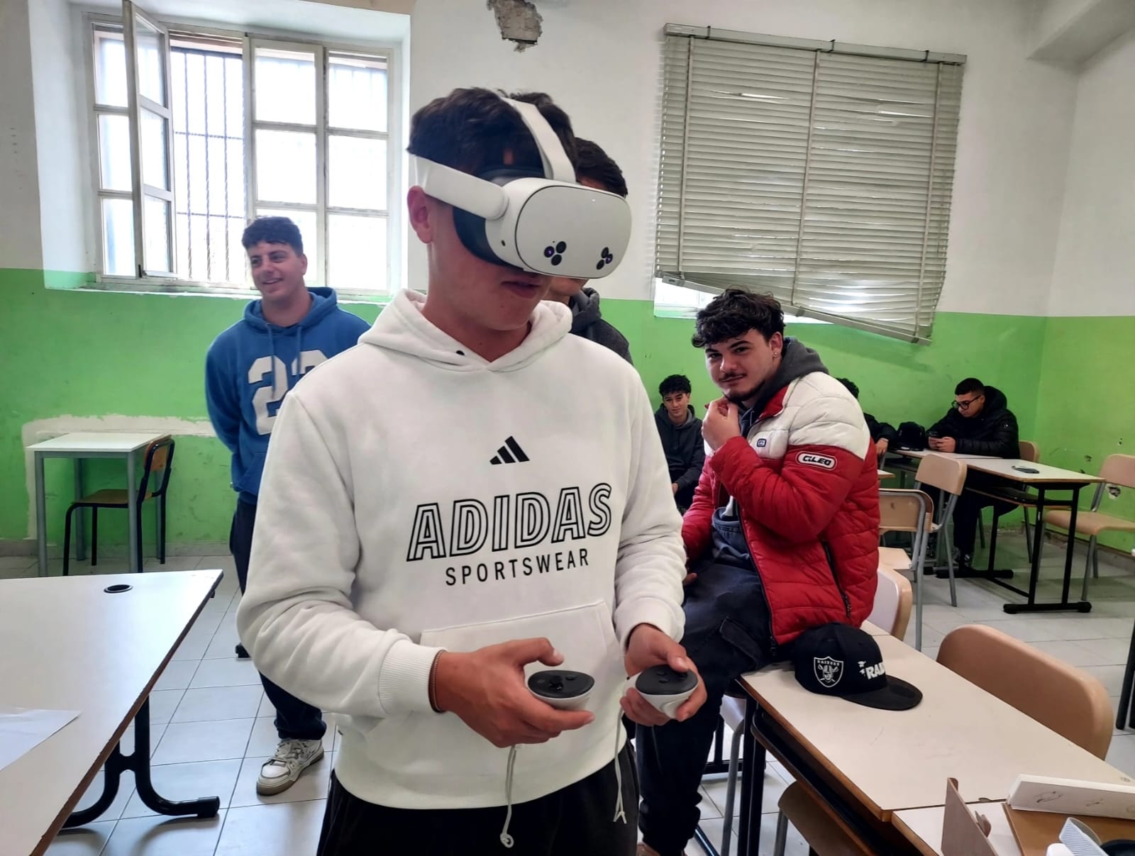 Student using a VR headset and controllers while classmates look on during the Long-Term Teaching/Learning Assignments in Naples
