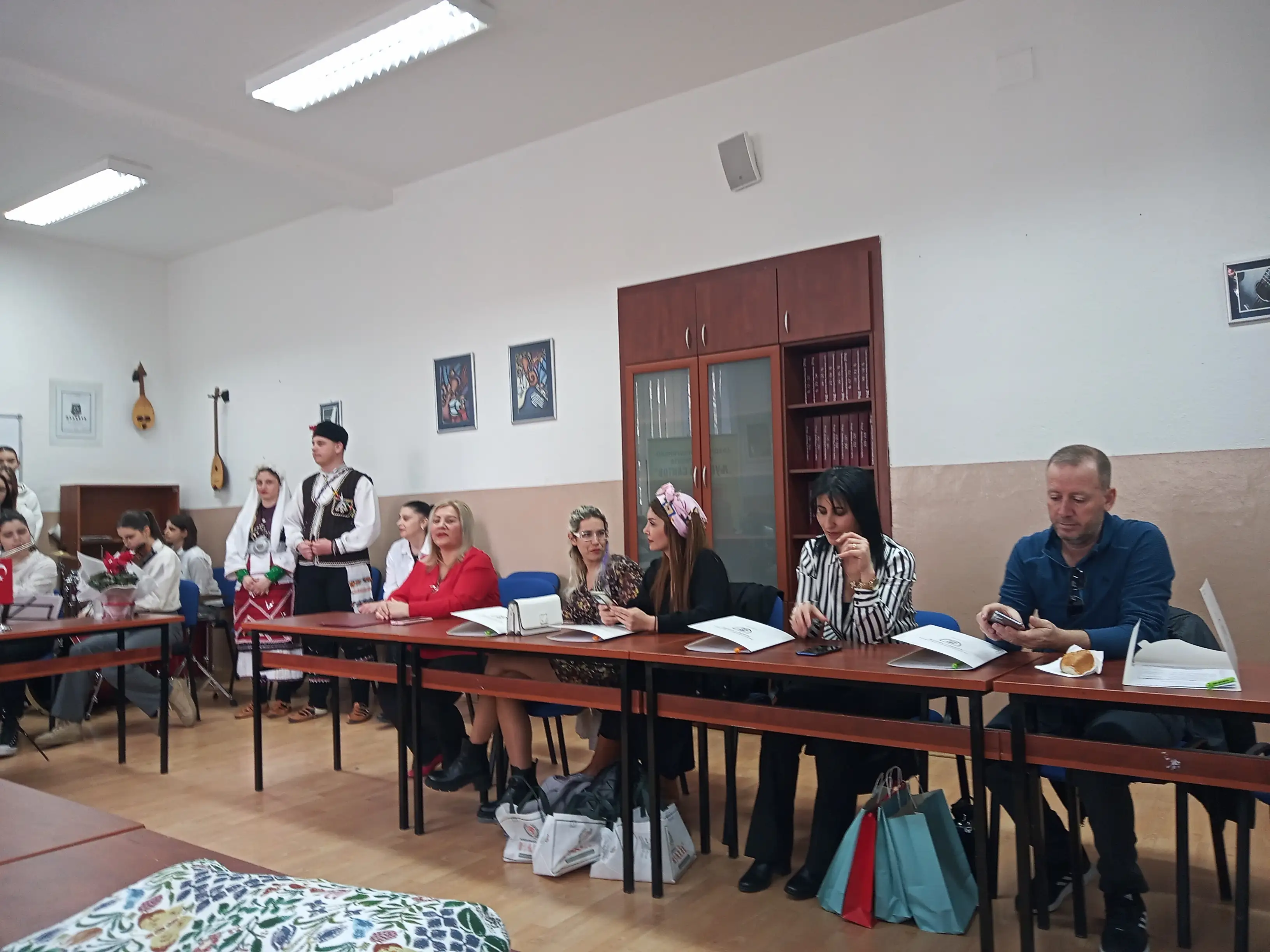 Community & English partners seated at the meeting tables, with students in traditional dress in the background, during the Kick-Off Meeting in Kočani