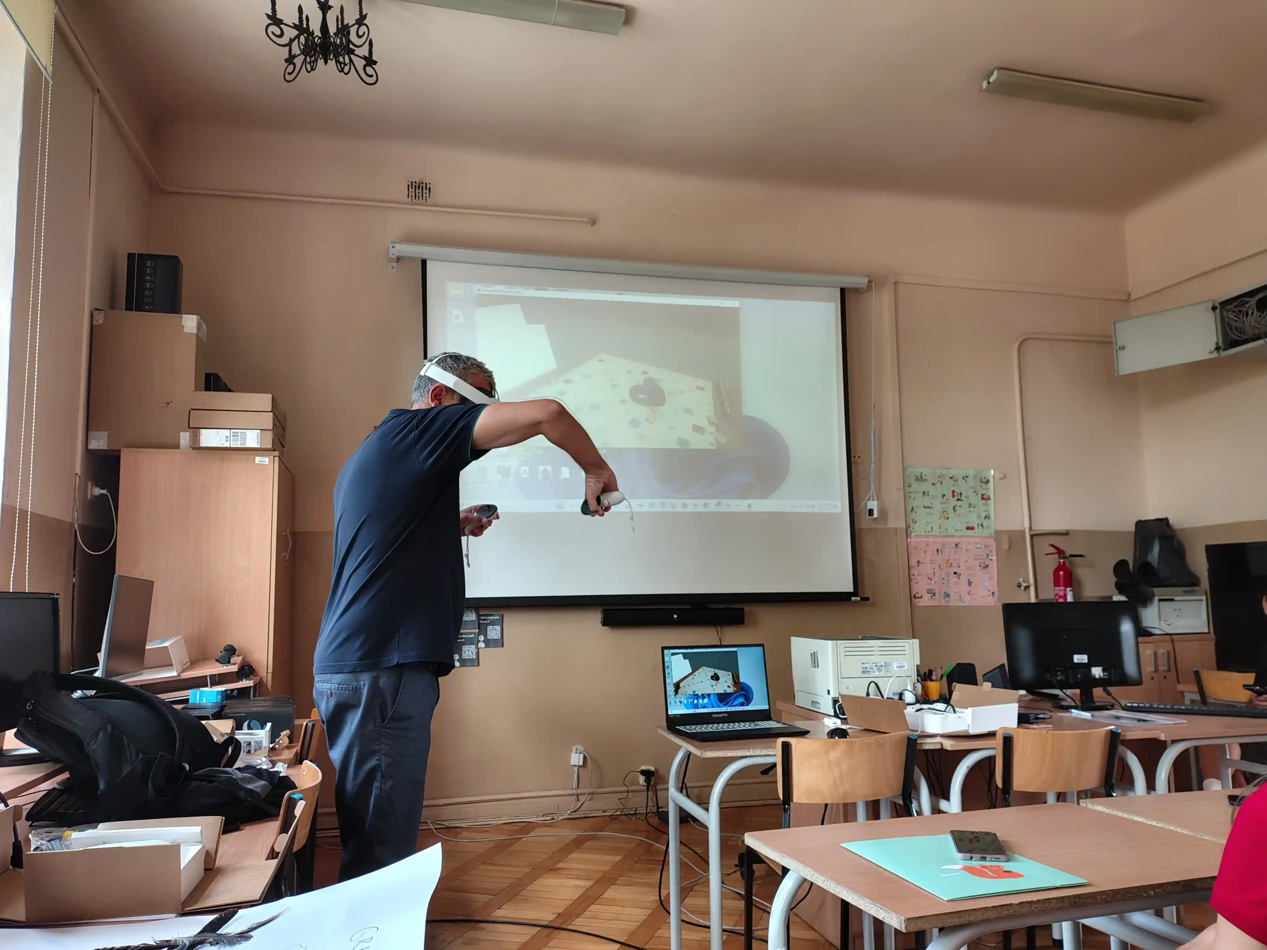 Trainer demonstrating a VR headset and controllers with the virtual view projected on screen during the first Community & English training in Radom